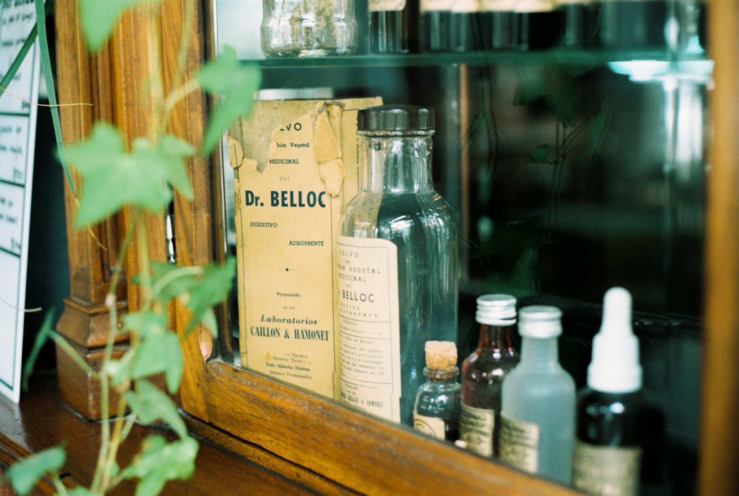 A collection of vintage apothecary glass bottles in a wooden cabinet.